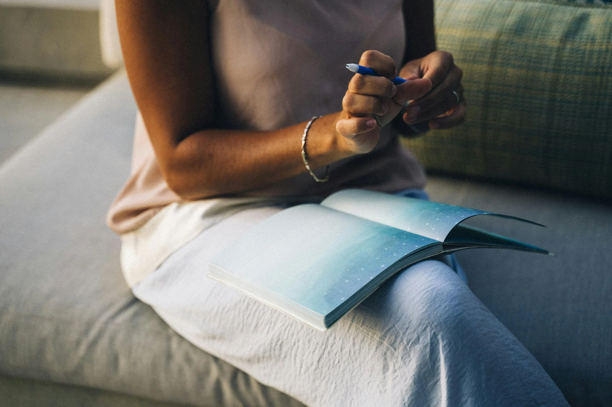 Woman holding a notepad and uncapping a pen as she prepares to write during a reflective moment.