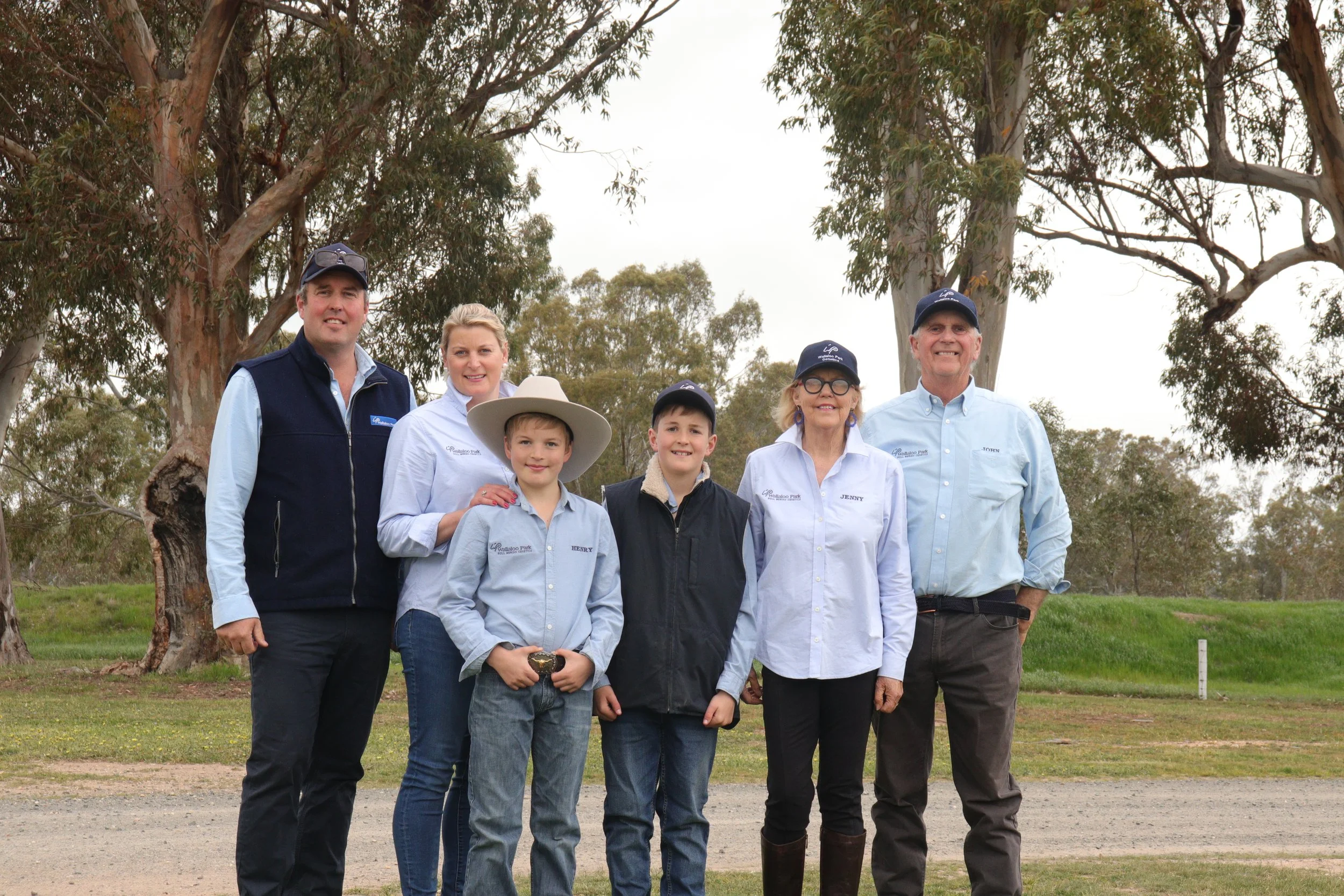 Group of six people standing outdoors in front of trees, smiling and looking at the camera.