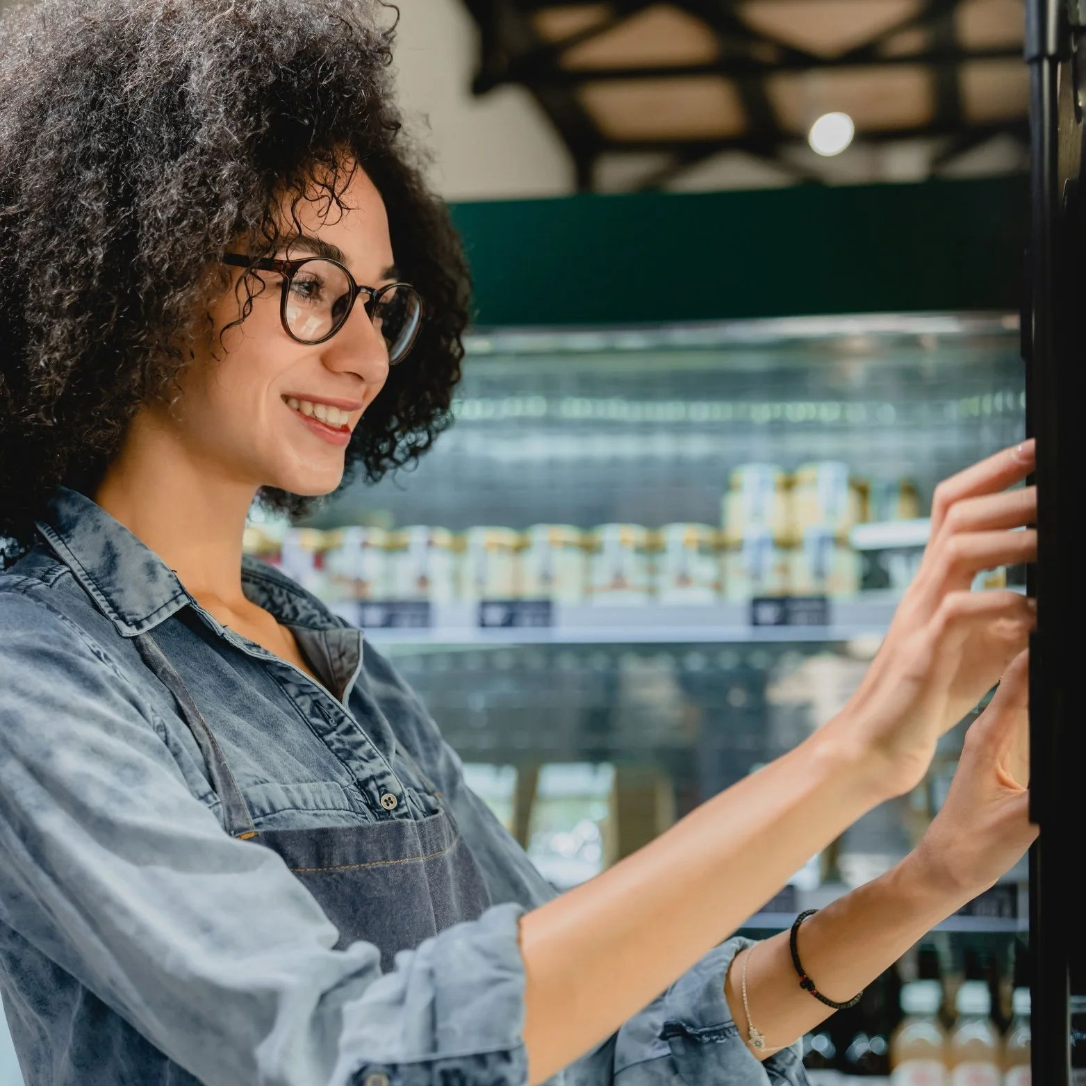 A woman with curly hair and glasses smiling while operating a vending machine.