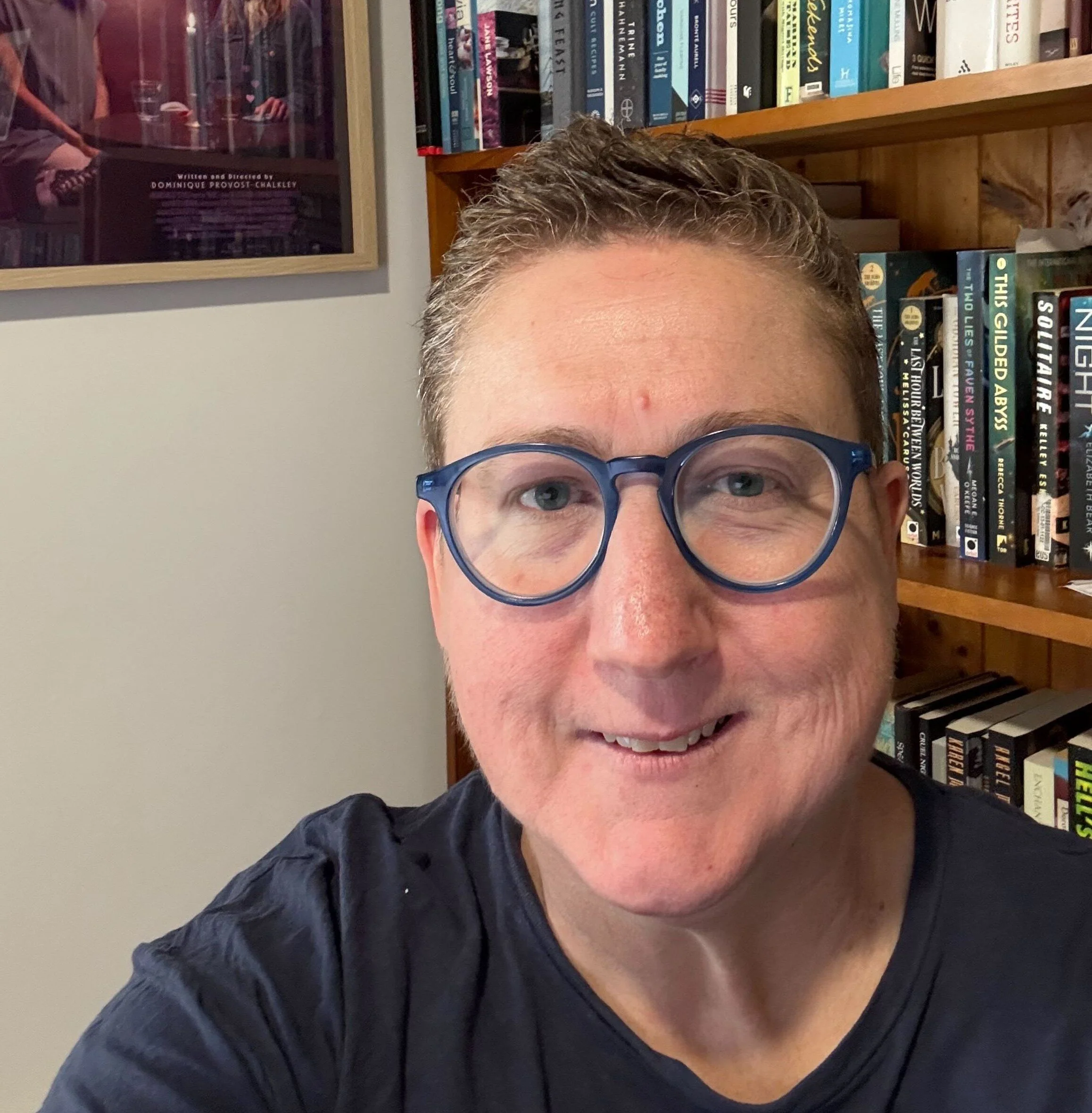 A portrait of Publisher v Holmes in front of a wall of books