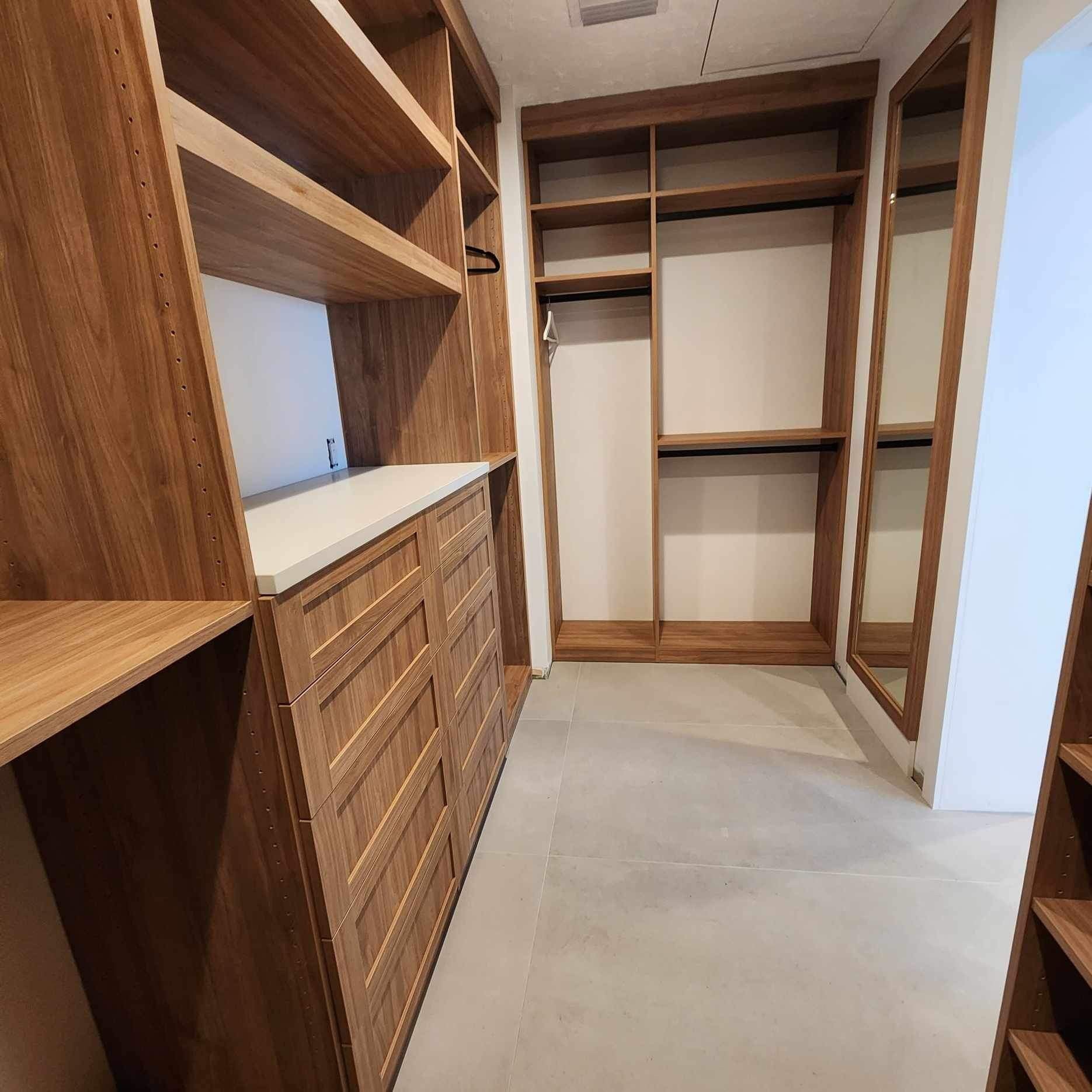 Empty walk-in closet with wooden shelves, drawers, and open hanging space, with a full-length mirror on the right side.