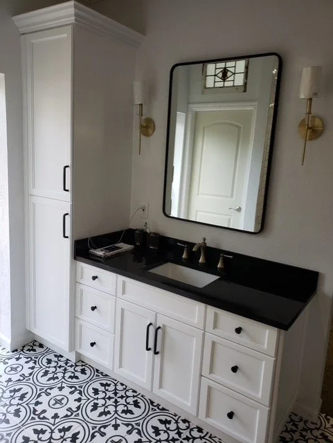 Bathroom vanity with a black countertop, white cabinetry, a large mirror, and two wall-mounted gold and white light fixtures.