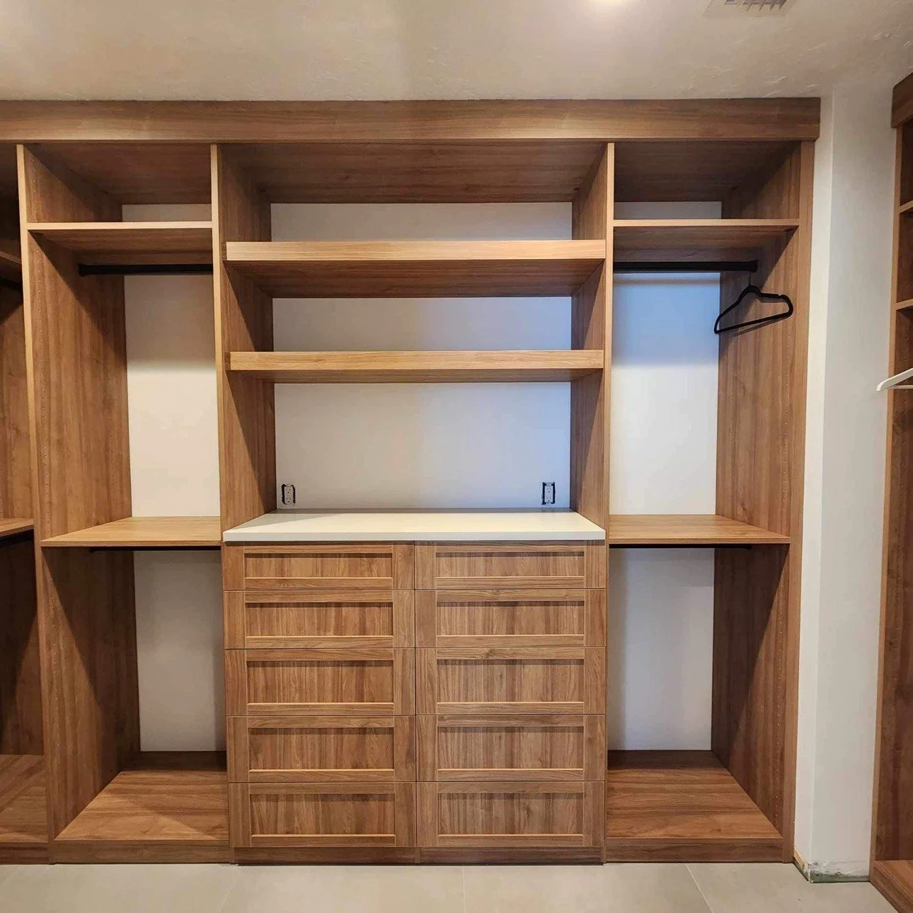 Empty custom-built wooden closet with multiple open shelves, drawers, and hanging space, with a white countertop.
