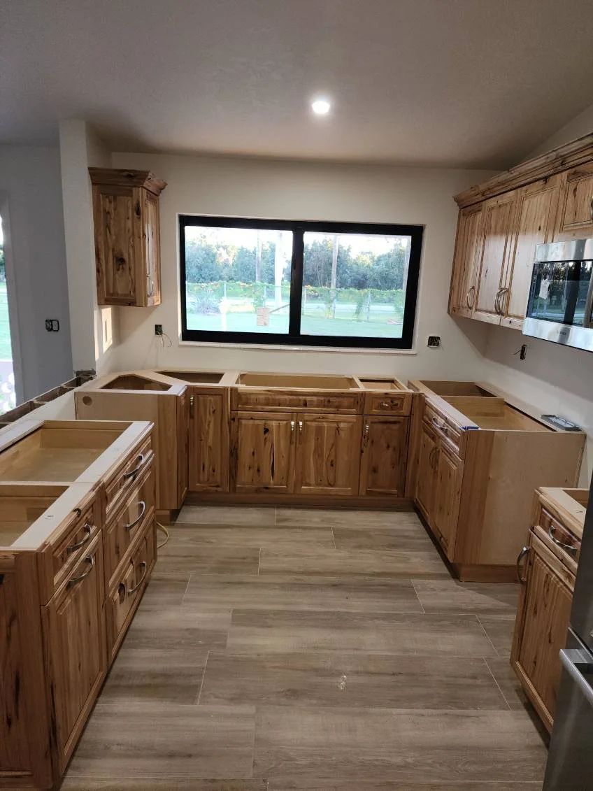 Kitchen with wooden cabinets and drawers, no appliances installed yet, large window overlooking outdoor area, and tile flooring.