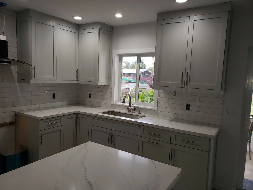 Kitchen with gray cabinets, white marble countertop, under-sink window, white subway tile backsplash, and recessed lighting.