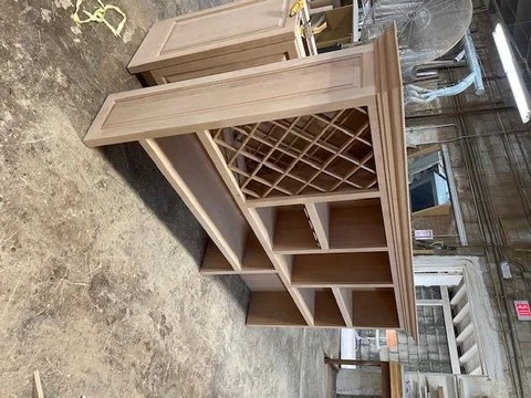 Wooden wine rack with cubby storage and a tall cabinet section, placed in a workshop or storage area.