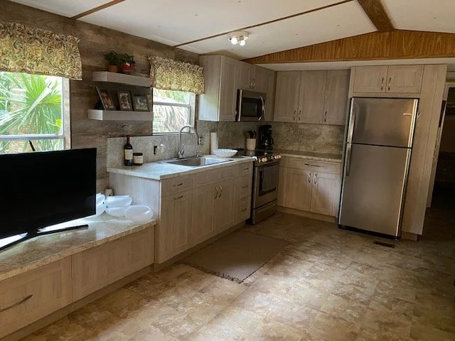 Kitchen with wooden cabinets, stainless steel fridge, stove, microwave, double sink, and window with floral curtains.