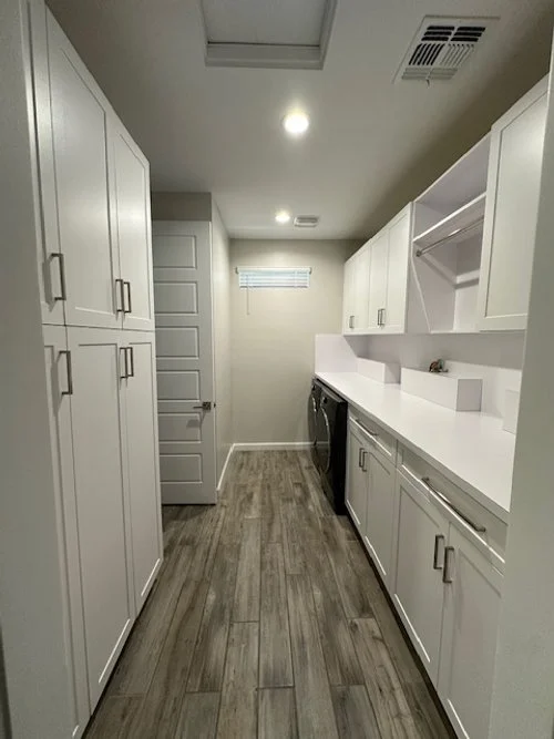 A laundry room with white cabinets and countertops, a washing machine, and a small window at the back.