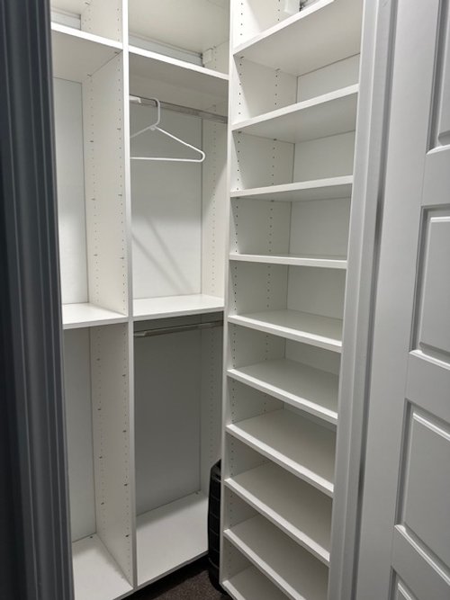 Empty white closet with shelves and hanging rod, showing a mostly empty storage space.