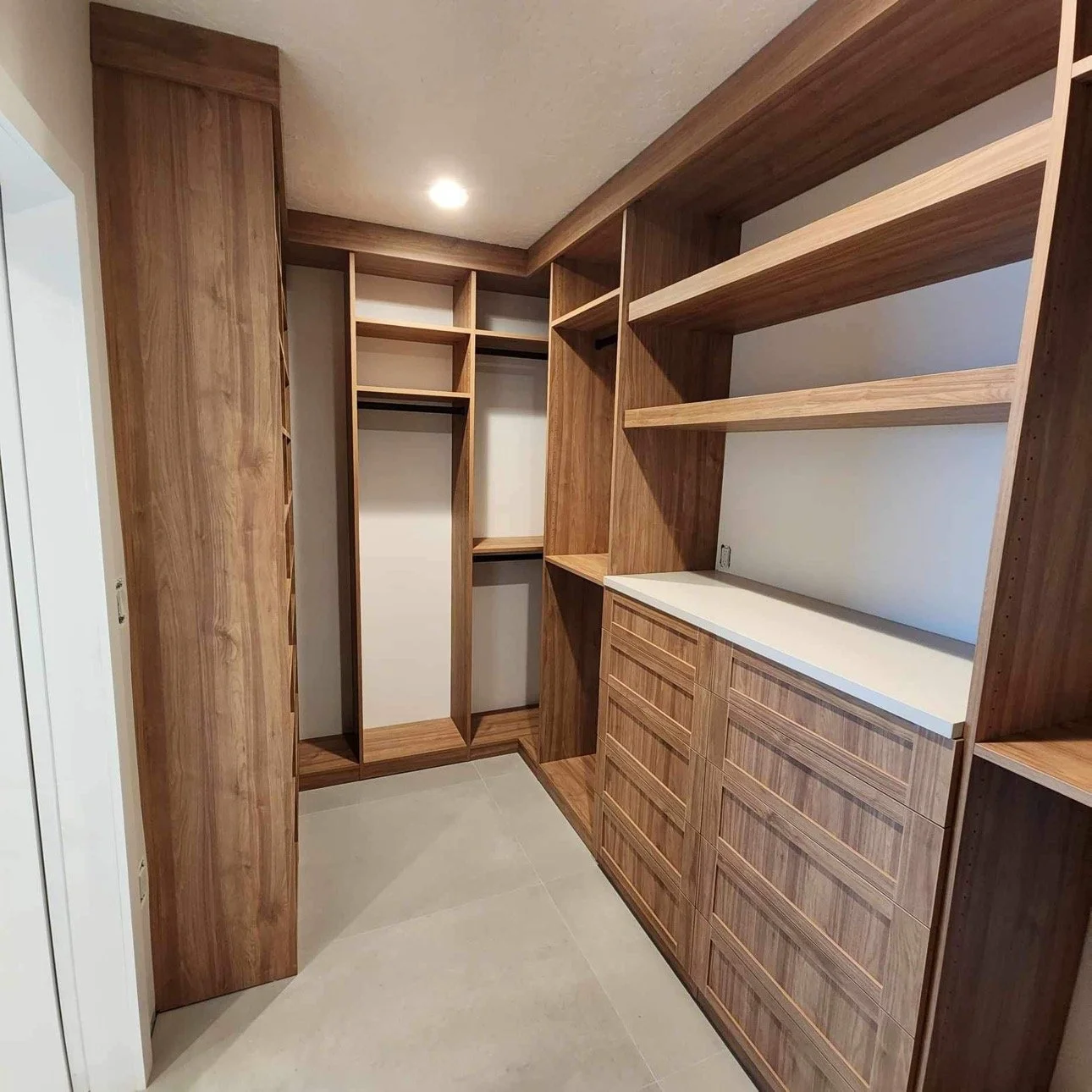 Empty wooden walk-in closet with shelving, hanging rods, and drawers.