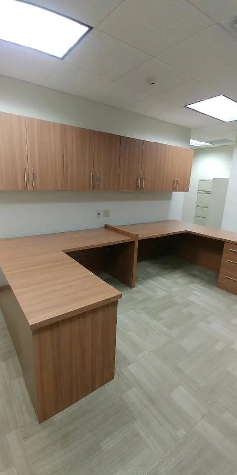 Empty office kitchen or break room with wooden cabinets, a wooden countertop with a corner section, and tiled flooring.