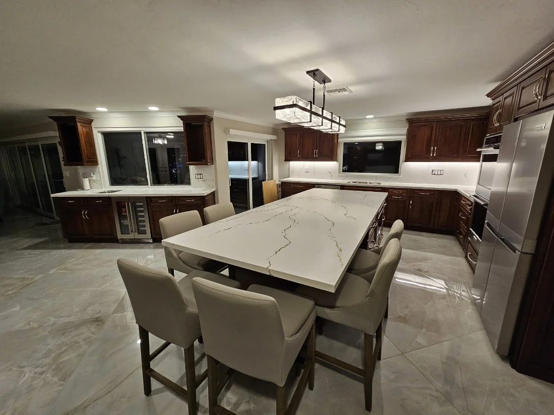 Modern kitchen with marble island, wooden cabinets, stainless steel appliances, and a chandelier overhead.