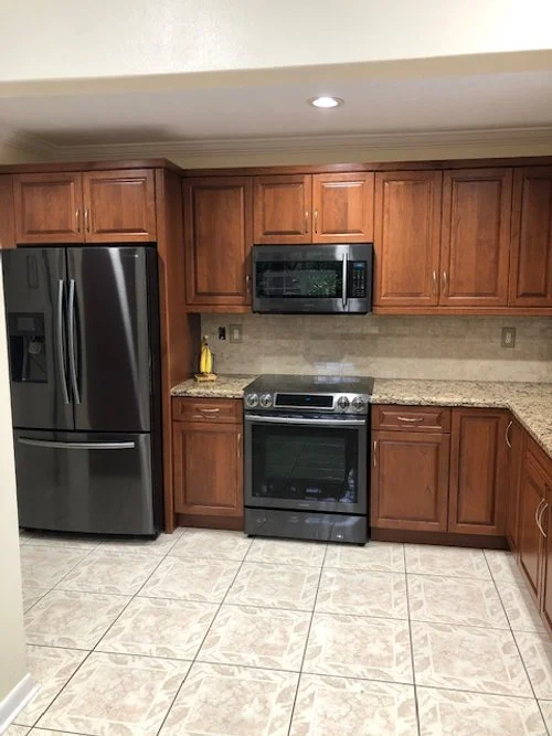 Kitchen with stainless steel refrigerator, microwave, and oven, wooden cabinets, granite countertop, and tiled floor.