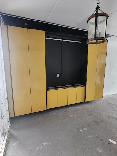 Yellow kitchen cabinets without appliances or a countertop, against a dark wall, under a hanging lantern-style light fixture.