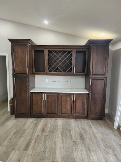 Dark wood kitchen cabinet with wine rack and countertop in a room with light wood flooring.