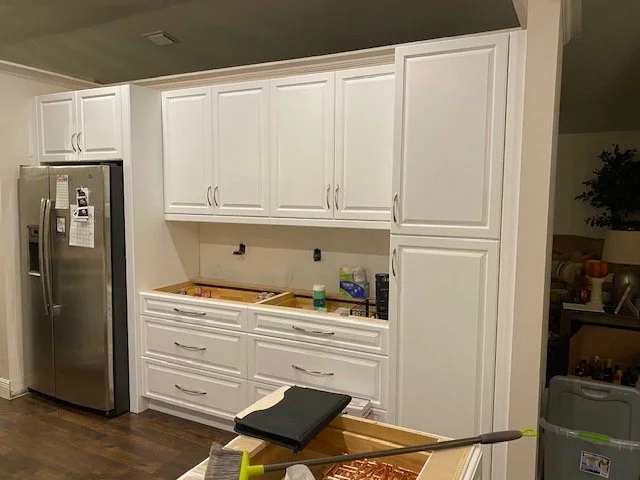 White kitchen cabinets and drawers with a stainless steel refrigerator, some tools, and a mop on the floor.