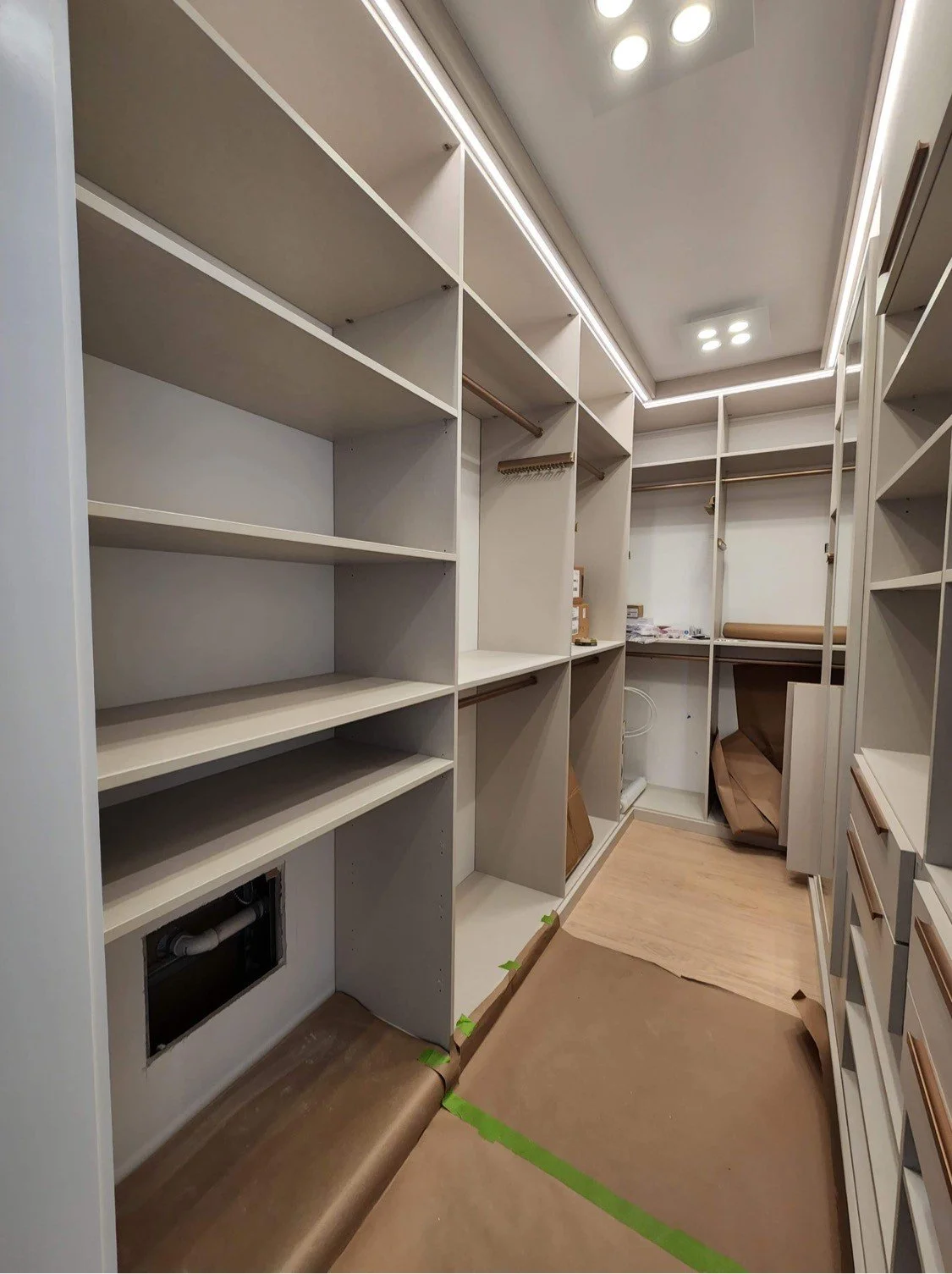 Empty walk-in closet with built-in white shelves and wooden accents, under construction or renovation.