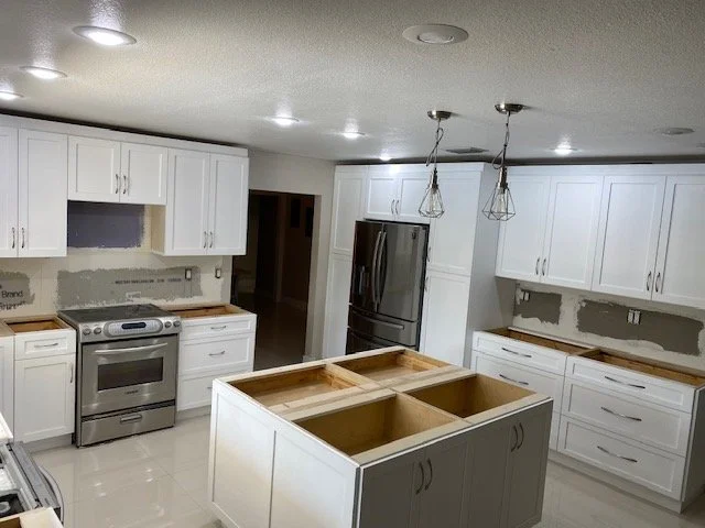 Kitchen with white cabinets, stainless steel refrigerator, oven, and a central island with no countertop, under construction or renovation.