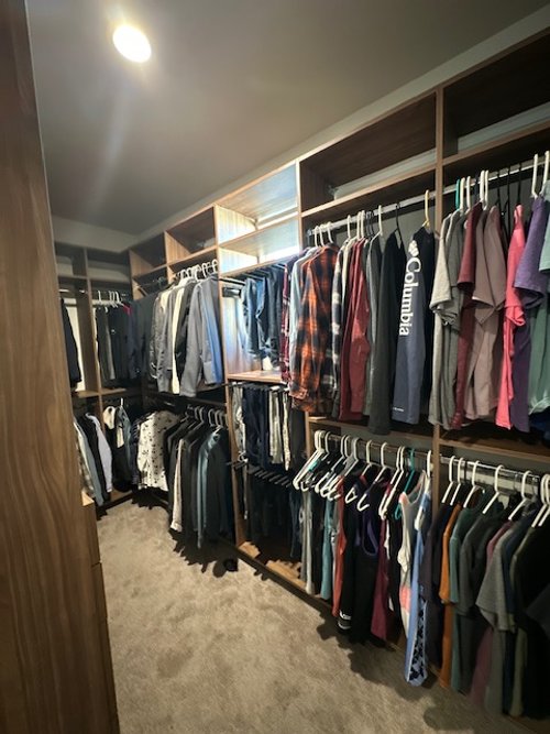 A walk-in closet with clothes hanging on wooden shelves and racks, organized by type and color.