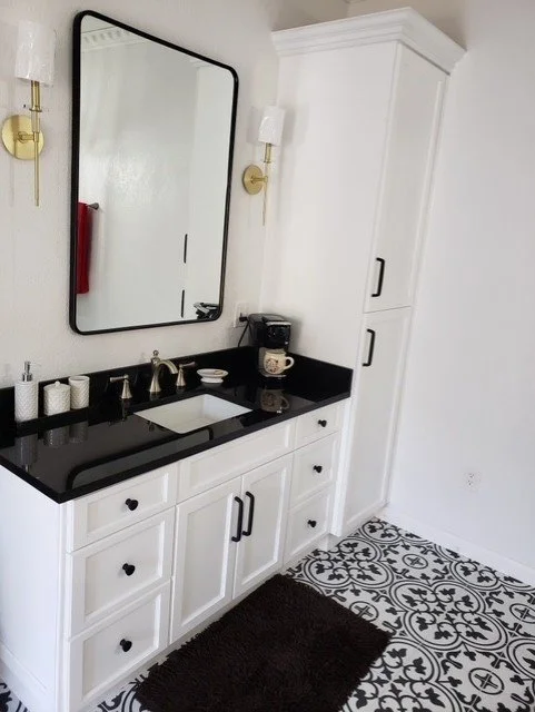 Bathroom vanity with white cabinets, black countertop, mirror, and wall-mounted light fixtures.