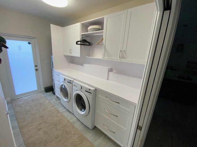 Laundry room with white cabinets, a countertop, a washing machine, a dryer, and open shelving with a few items.