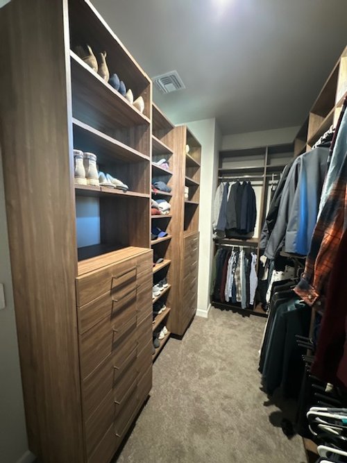 A walk-in closet with wooden shelves and drawers filled with shoes and clothes, including hanging shirts and jackets.