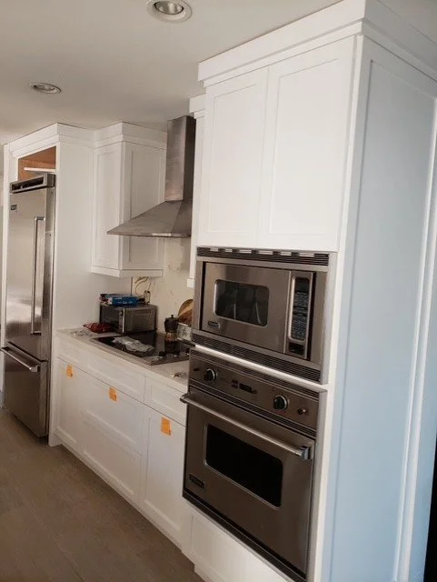 Modern kitchen with white cabinets, stainless steel refrigerator, built-in microwave, and oven.