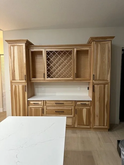 Kitchen cabinet with multiple drawers and storage compartments, including a wine rack, made of light wood, with a white countertop.