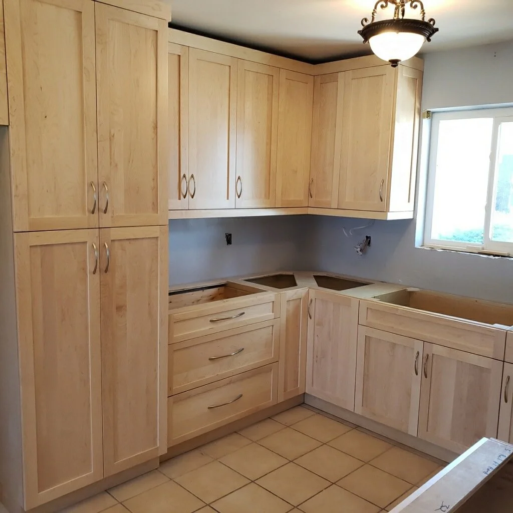Kitchen cabinets installed with light wood finish, a tiled floor, a window, and a ceiling light fixture, with some areas under construction.