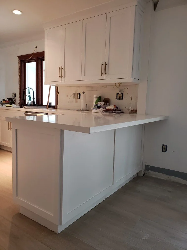 Partially finished kitchen with white cabinets, a countertop, a window with a wooden frame, and some construction tools and materials.