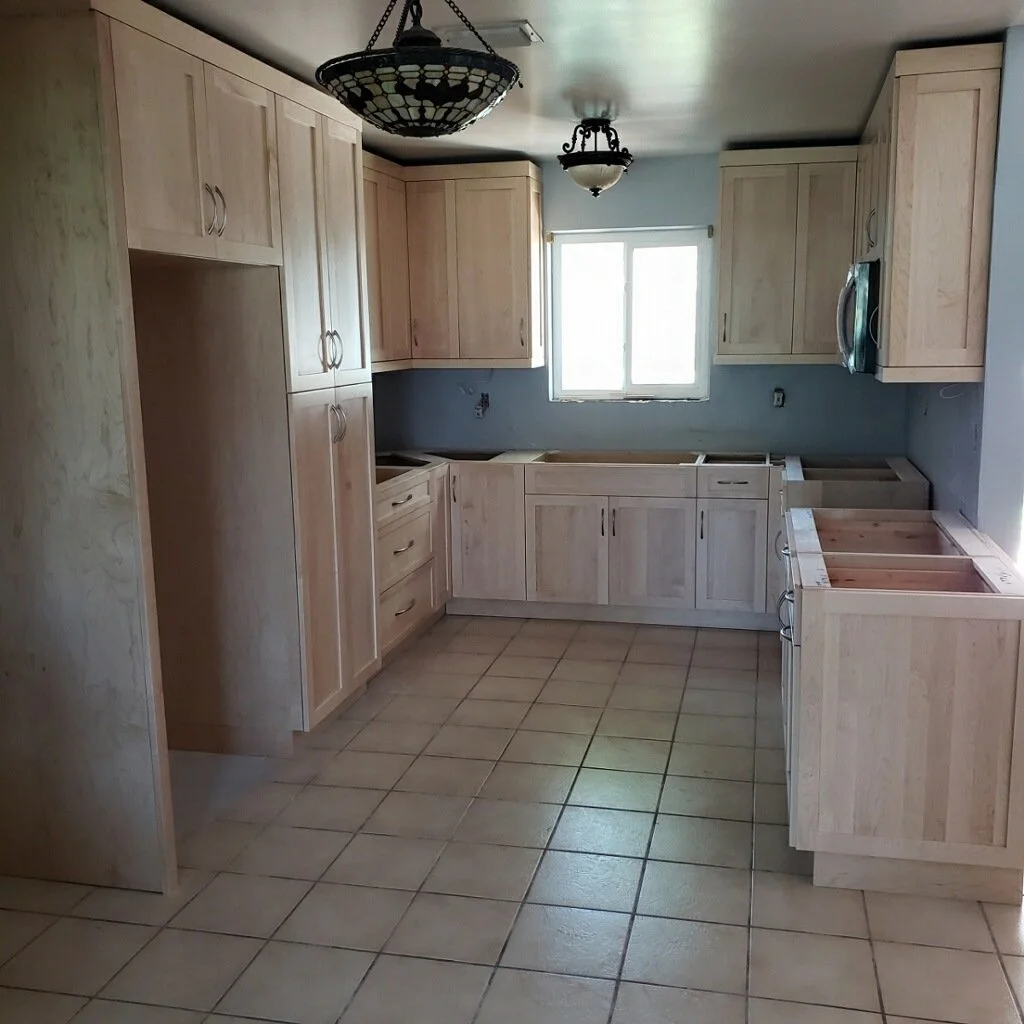 Unfinished kitchen with light wooden cabinets, a window, and tiled floor, hanging light fixture, and a microwave installed on the upper right corner.
