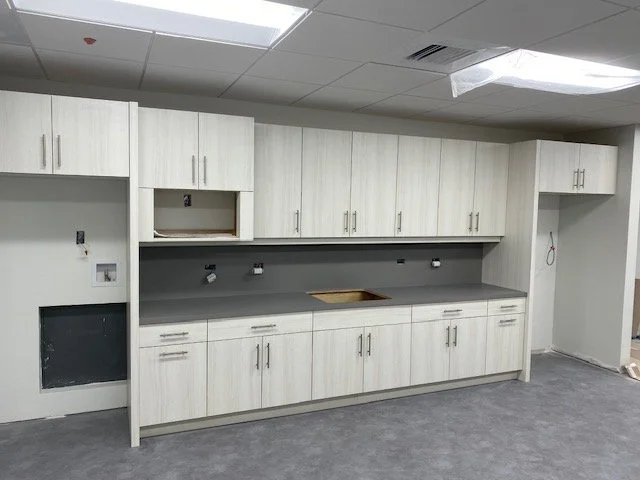 Empty kitchen with white cabinets, gray countertop, and unfinished wall with electrical outlets.