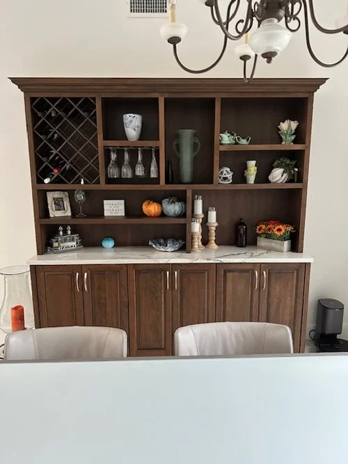 A wooden hutch with a white marble top displays various decorative items, including vases, pumpkins, candles, and flowers, in a dining room.