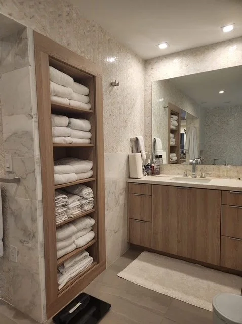 Bathroom with a wooden shelf filled with neatly folded white towels and a vanity with a large mirror, sink, and bathroom essentials.