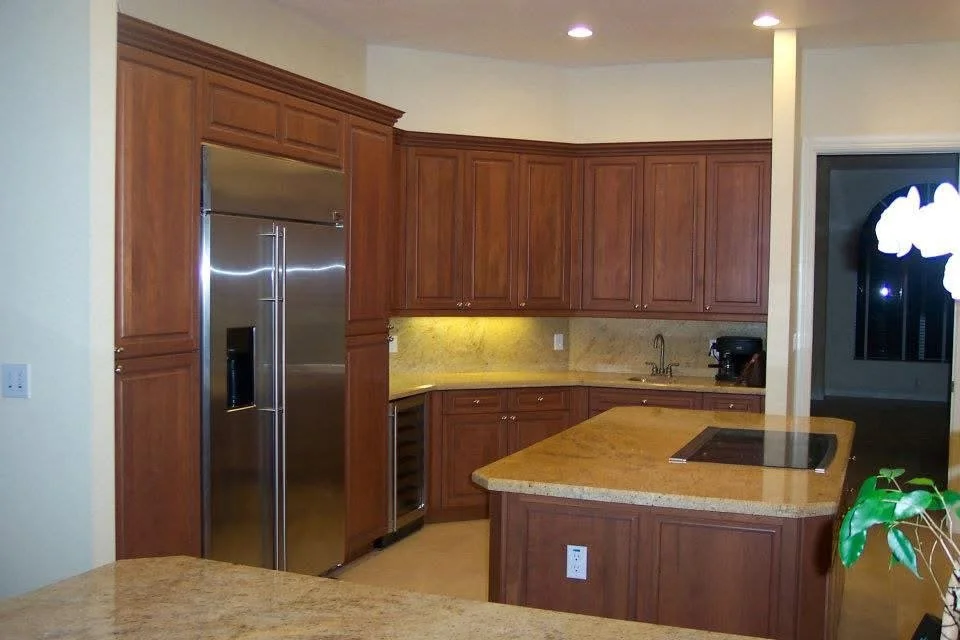 Kitchen with wooden cabinets, a stainless steel refrigerator, cream-colored countertops, and a built-in stovetop.