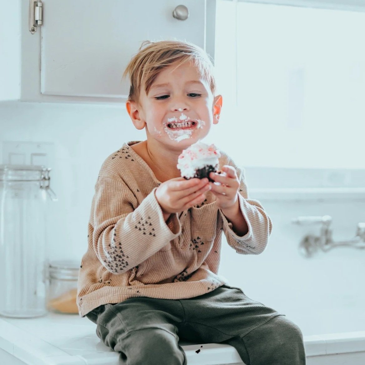 A young boy with mud on his face and a cake in his hands, smiling with cake and frosting on his face.
