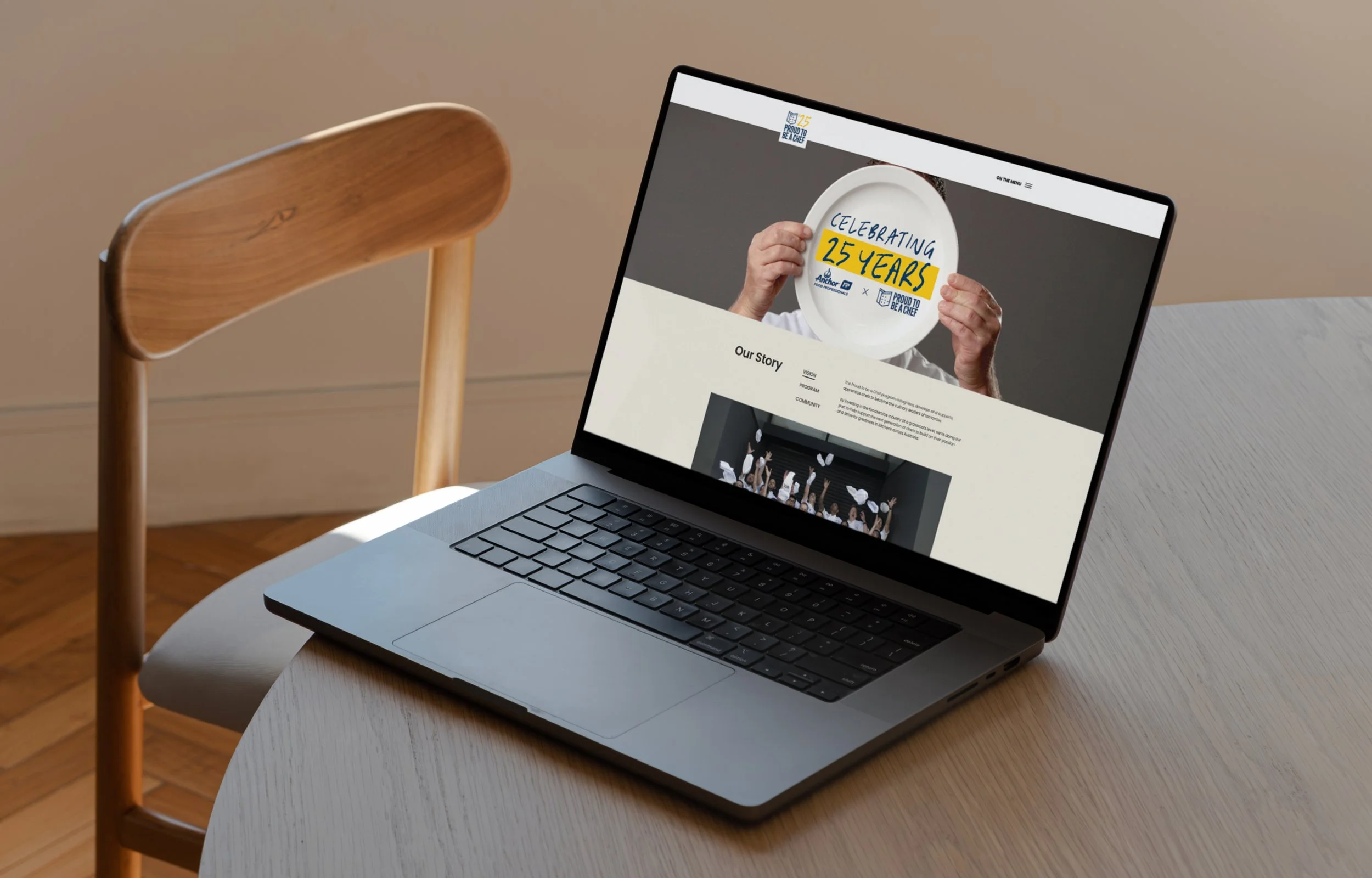 Laptop on a light-colored table displaying a webpage celebrating 25 years with an image of a person holding a plate that says 'Celebrating 25 Years'.