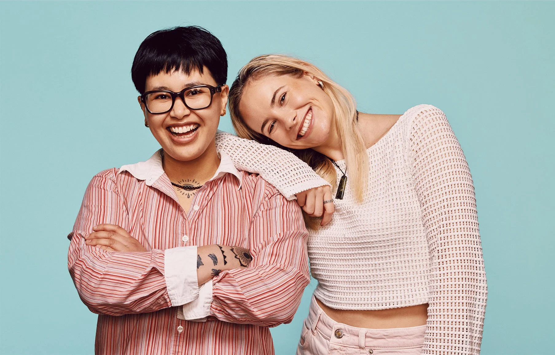 Two smiling women with their arms around each other standing against a light blue background.