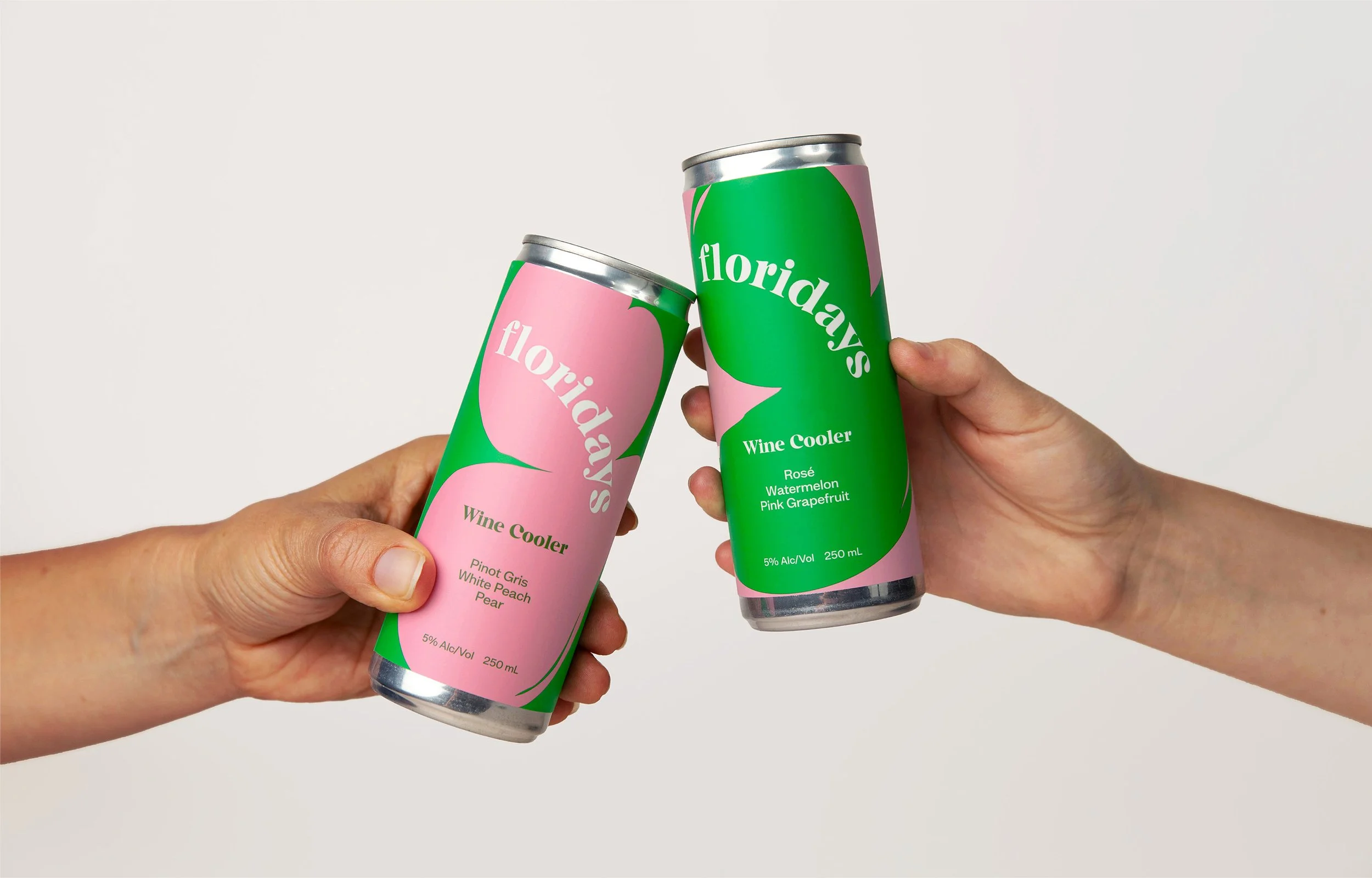 Two hands holding cans of Floridaays Wine Cooler, with one can pink and green labeled 'Pinot Gris, White Peach, Pear' and the other green and pink labeled 'Rosé Watermelon Pink Grapefruit', clinking against a plain white background.