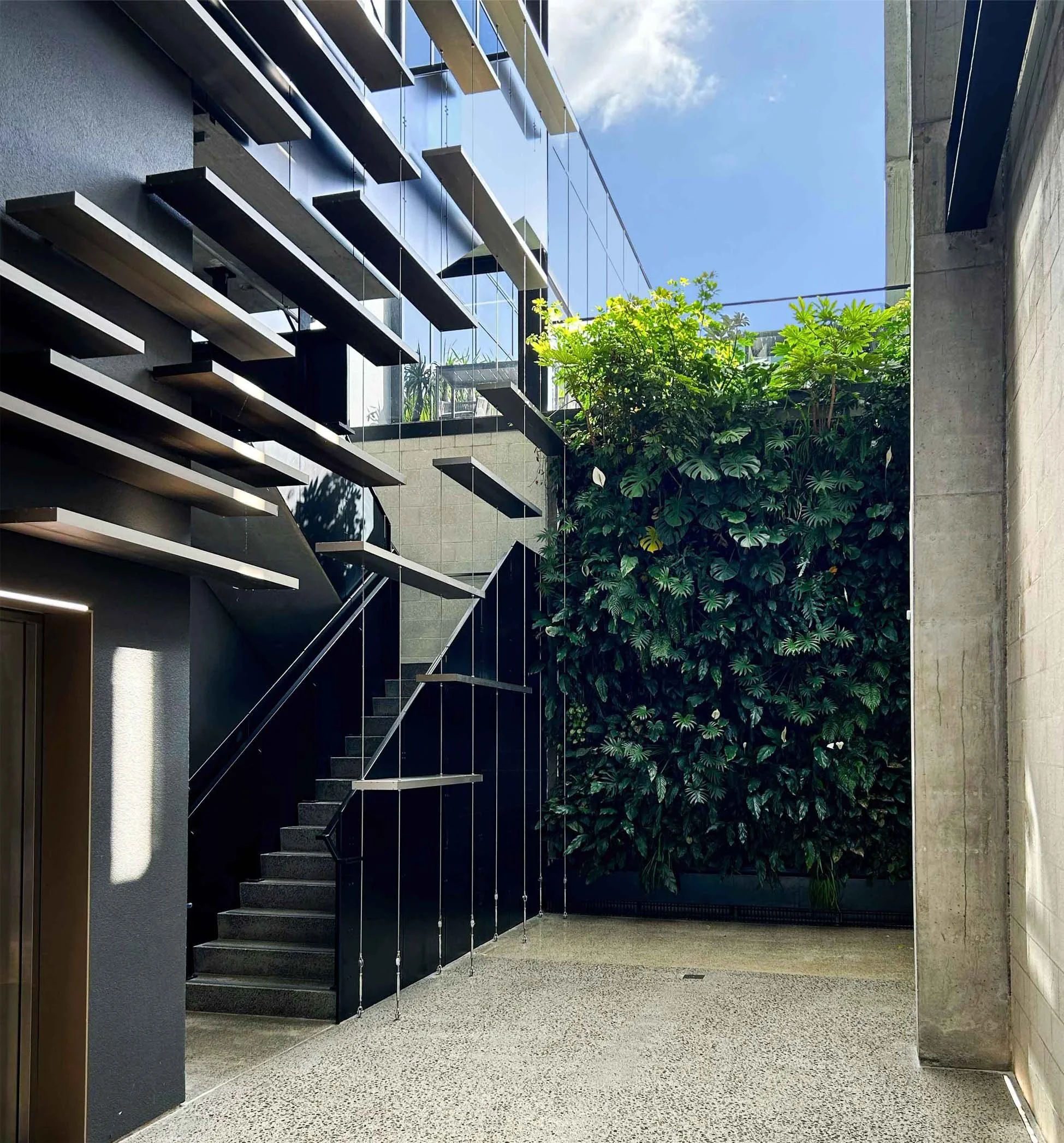 Modern building interior with an outdoor staircase, a green wall, and glass windows reflecting the sky.