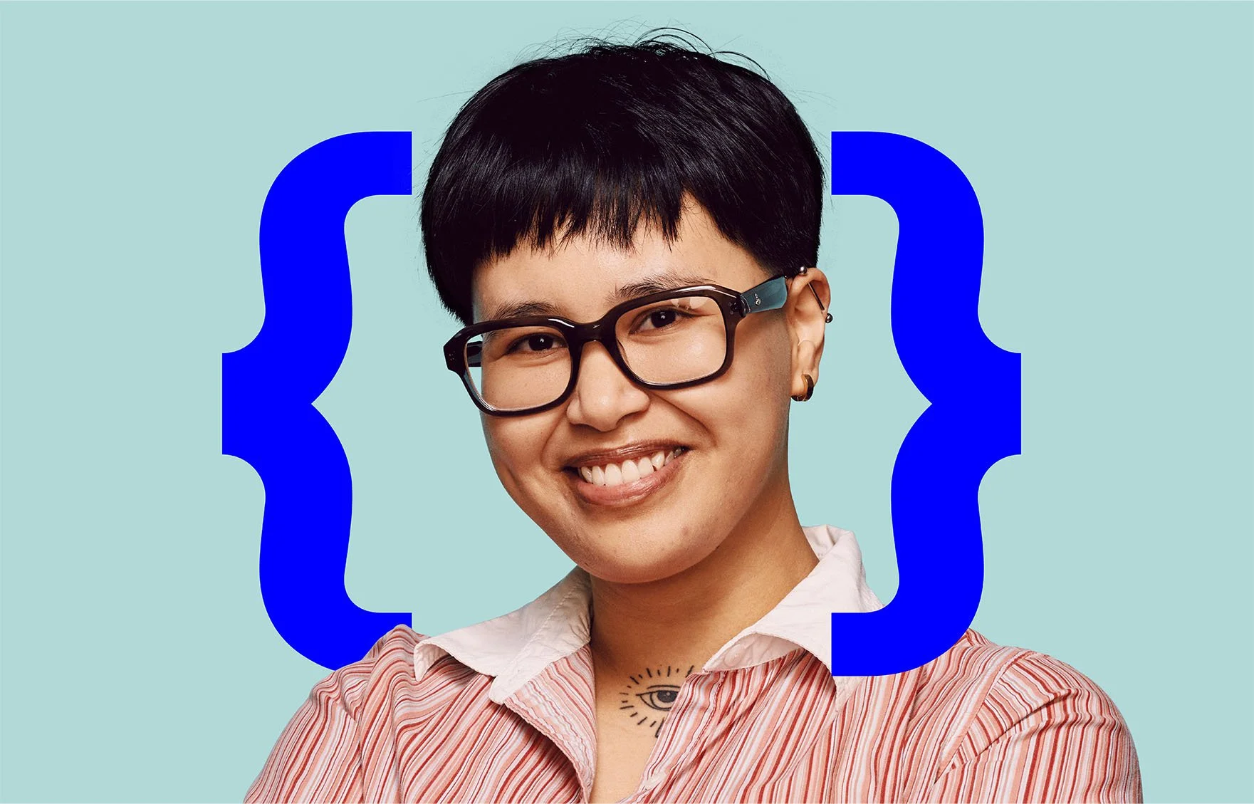 A young woman with short black hair, glasses, and a small tattoo of an eye on her chest, smiling against a light blue background with large blue curly brackets on either side.