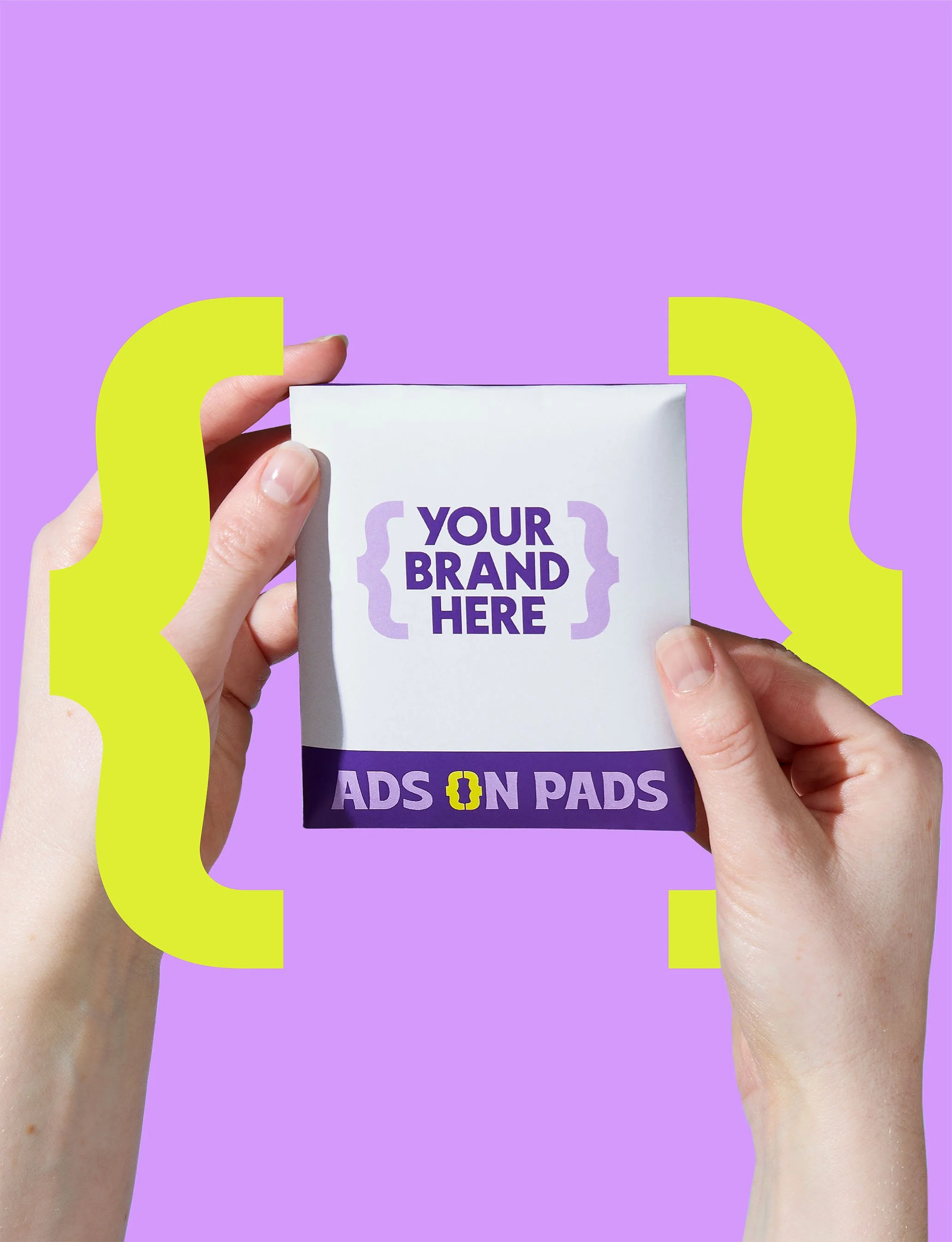 Two hands holding a box with placeholder text 'Your Brand Here' and 'Ads on Pads' on purple and white packaging against a purple background with yellow brackets.