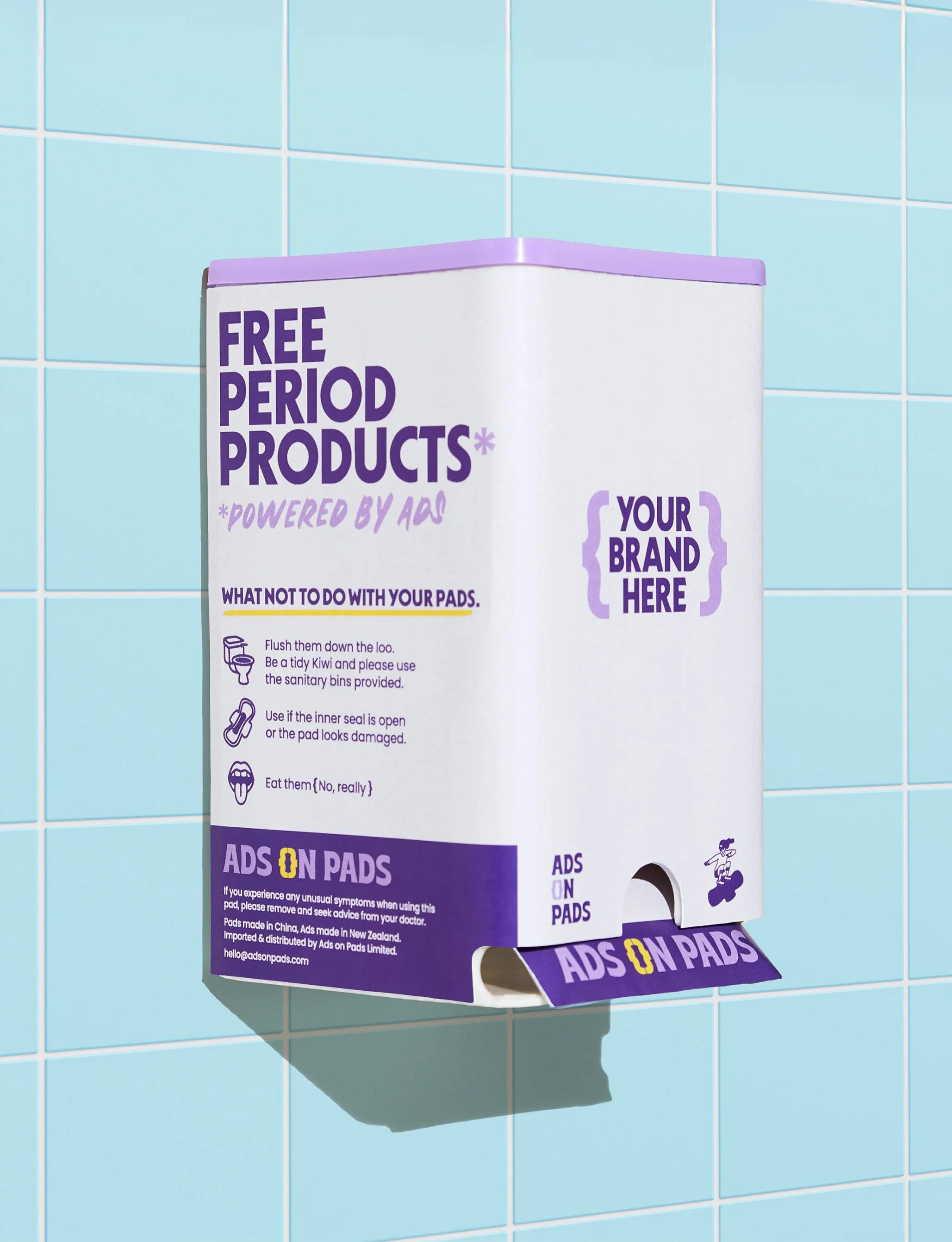 A sanitary product dispenser on a light blue tiled wall, advertising free period product samples with humorous instructions and branding.