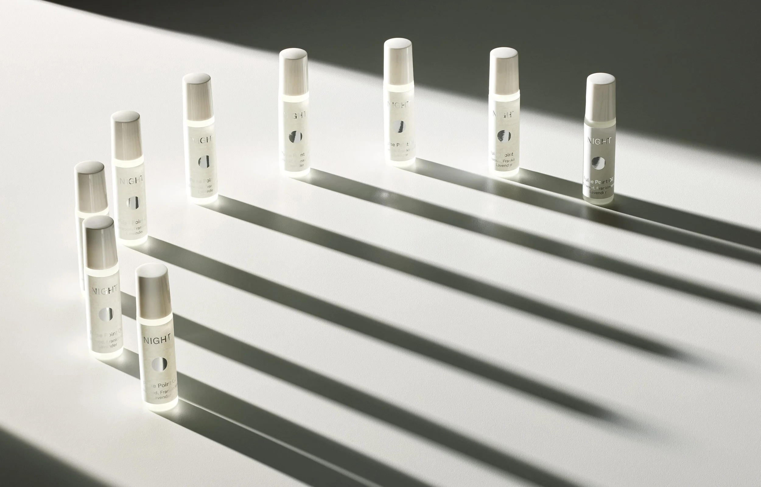 Several small white bottles arranged on a light surface, casting long shadows from sunlight.