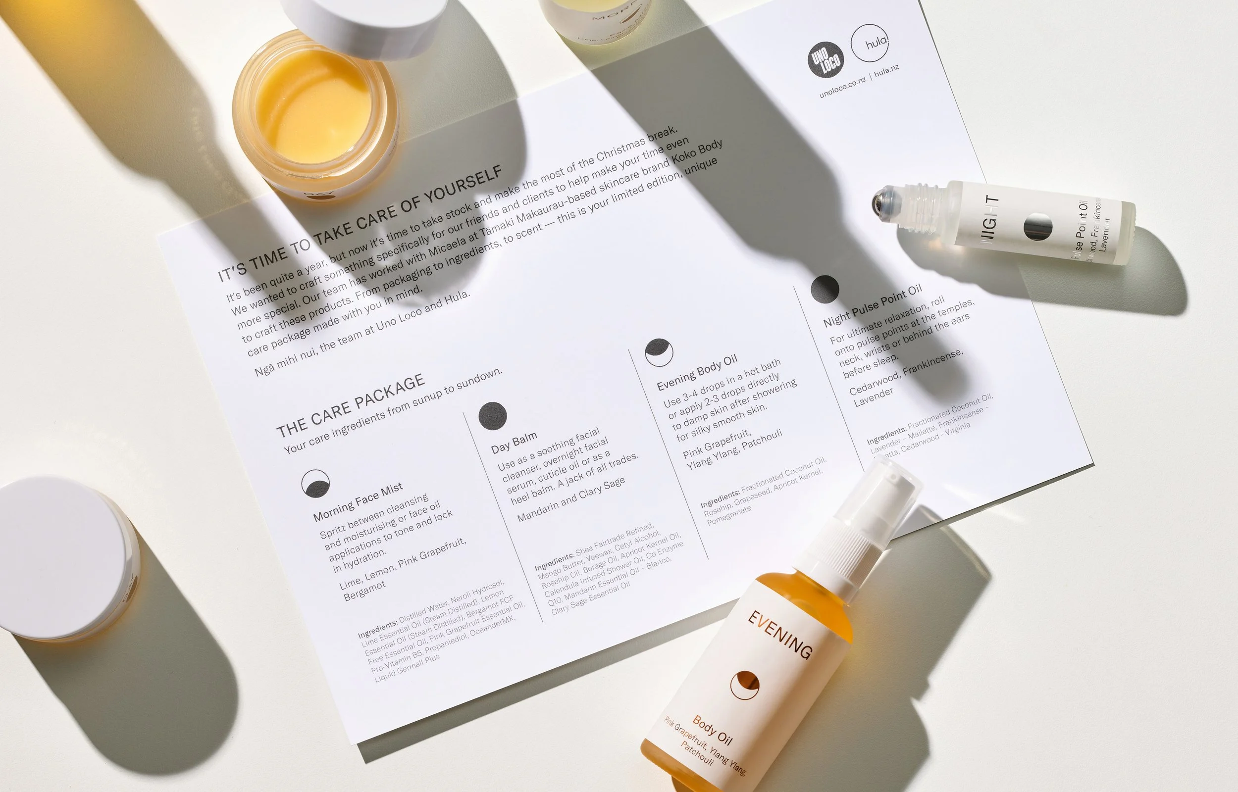 A skincare product advertisement layout on a white surface, featuring several containers of cream and sprays, along with a printed sheet describing a self-care routine with ingredients.