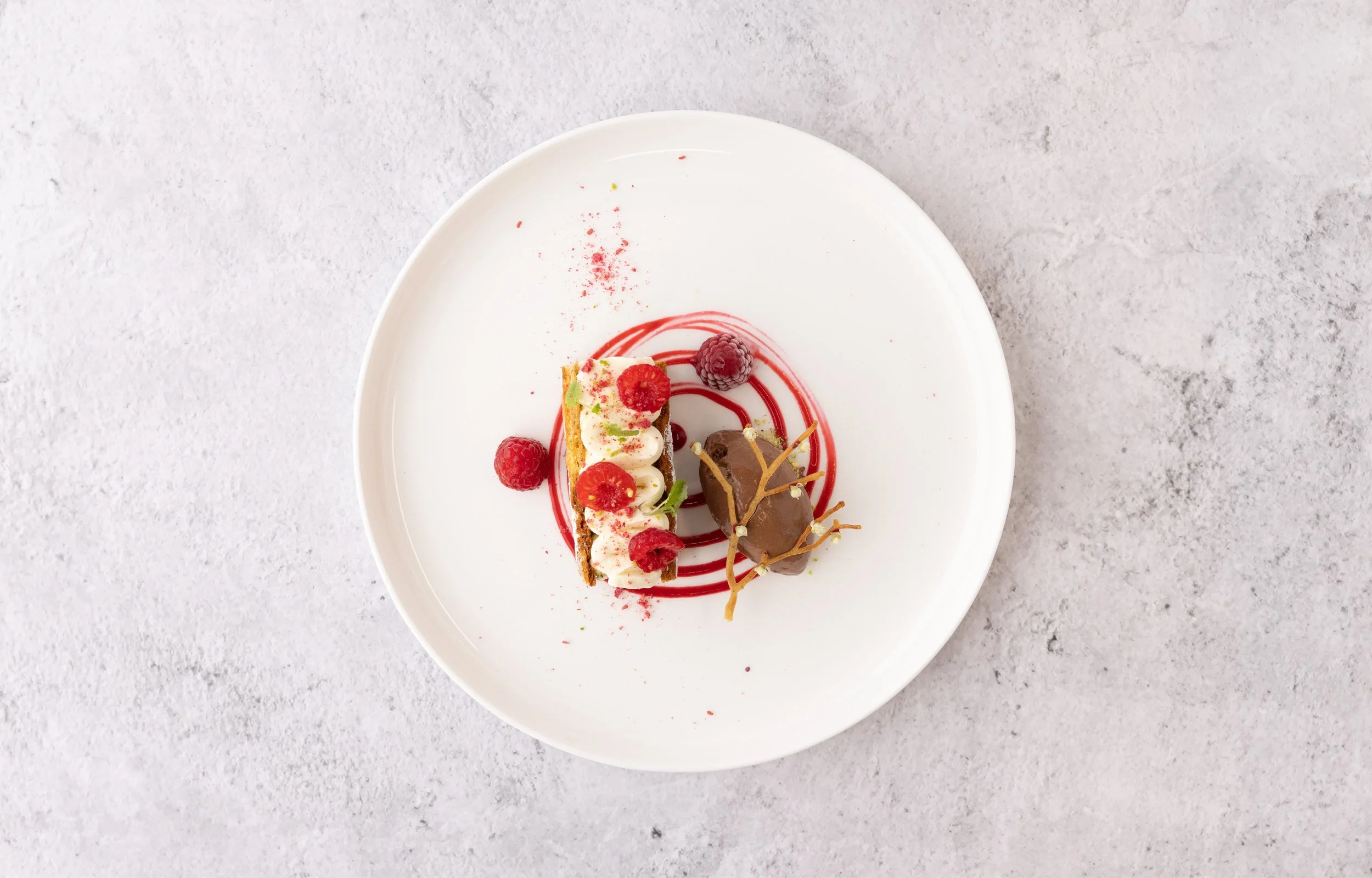 A plated dessert with raspberries, chocolate, and decorative sauces on a white plate