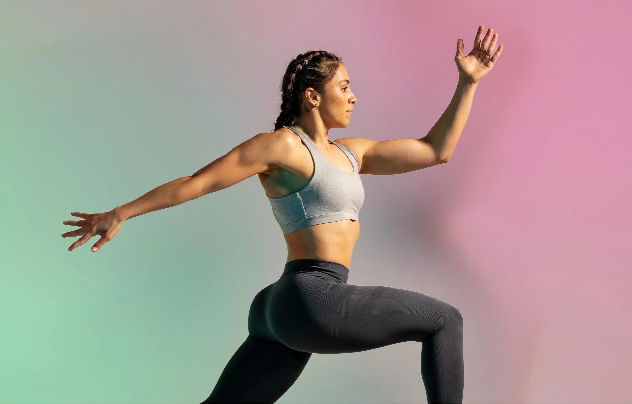 A woman in athletic clothing performs a yoga pose, kneeling with one arm extended forward and the other arm extended backward, against a colorful gradient background.