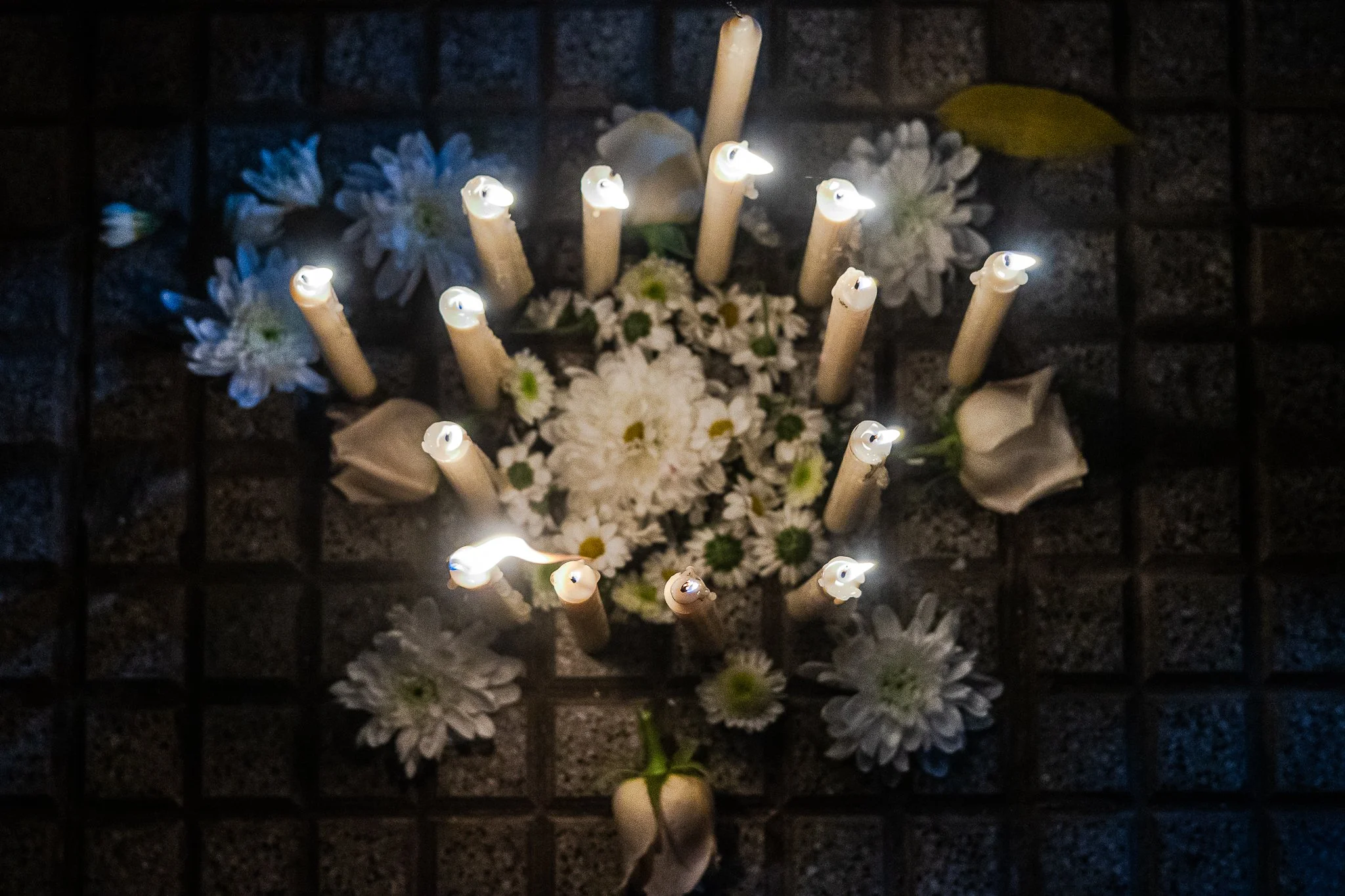 Velas y flores blancas colocadas en un altar con una reja de fondo, en una ceremonia religiosa o conmemorativa.