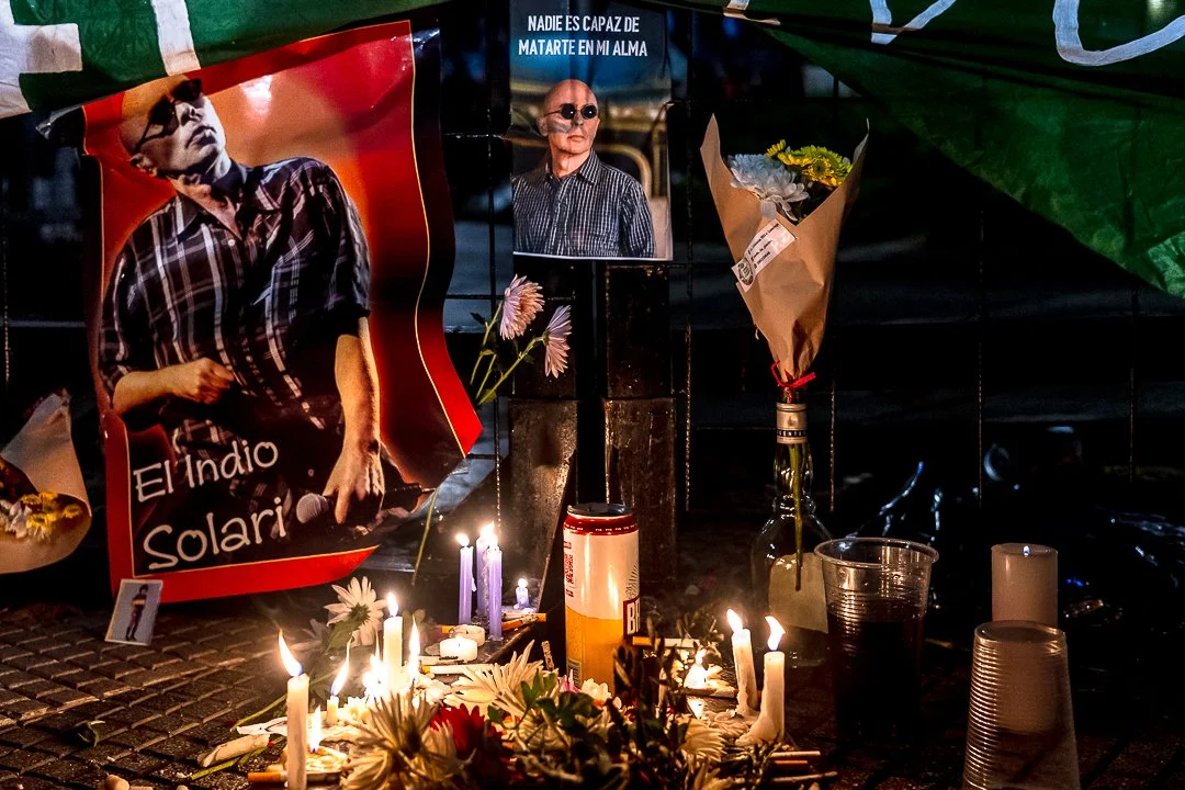 Un altar de homenaje con velas encendidas, flores, fotos de un hombre, y una pancarta que dice 'El Indio Solari'.