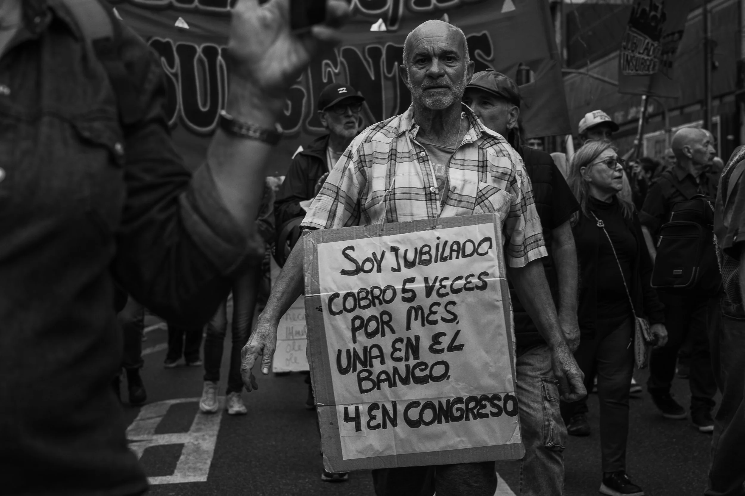 Personas participando en una manifestación, sosteniendo un cartel con texto en español, en una calle urbana.